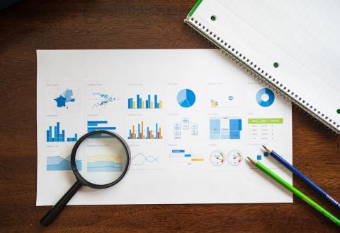 Image of a paper full of different charts. There are two pencils and a magnifying class next to the paper.